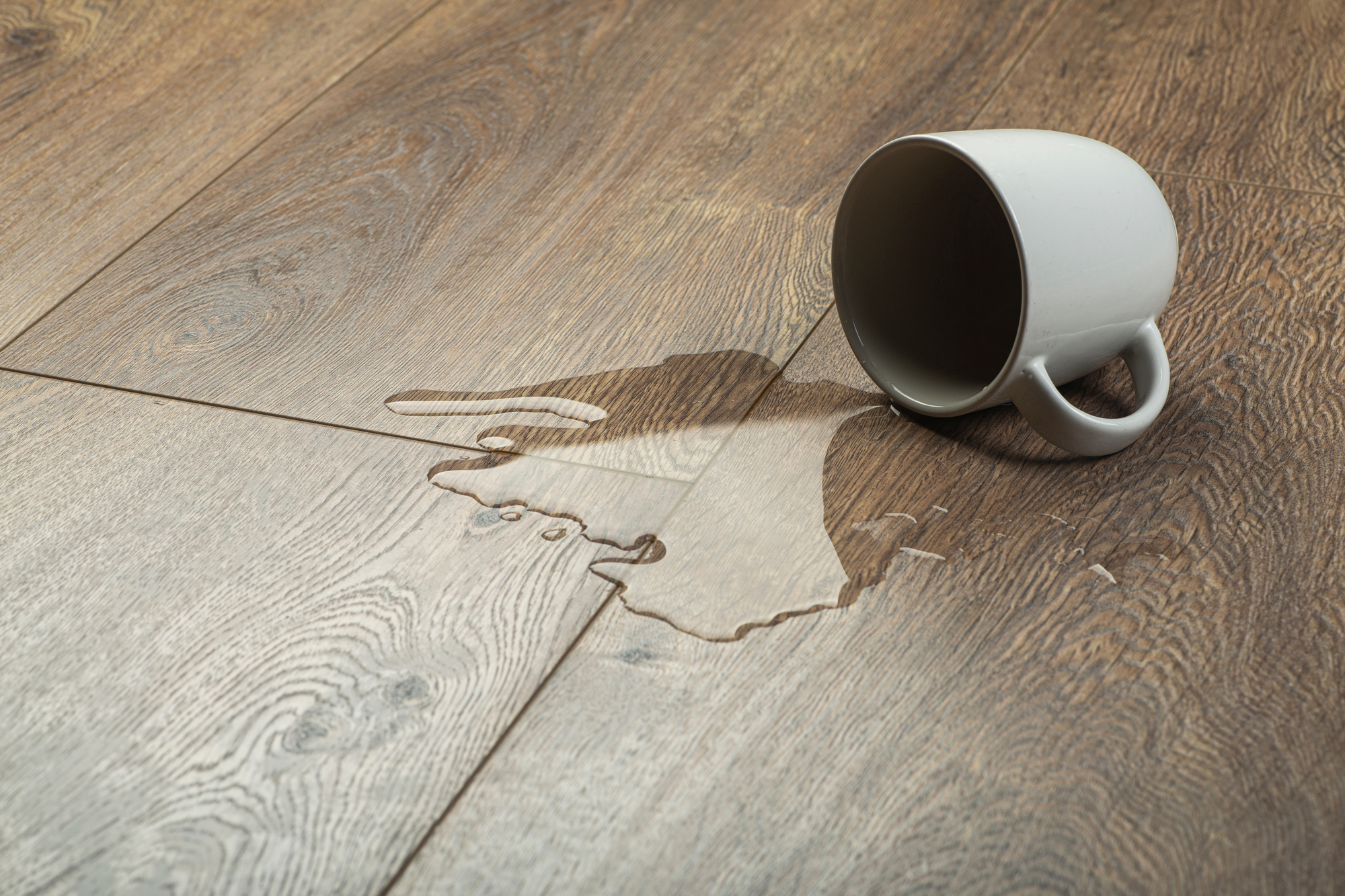 Umgekippte Tasse mit verschütteter Flüssigkeit auf Vinylboden